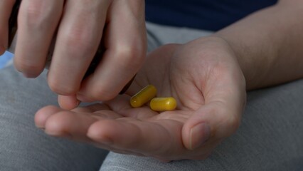 Two gelatin capsules with medicines are poured into the palm of your hand. Yellow capsules with drugs for the treatment of serious diseases. The high price of drugs and medicines.