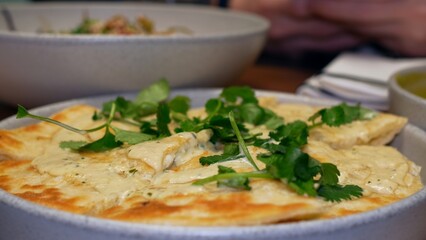 Pan-Asian cuisine, a plate with dishes on the restaurant table. Flatbread with cheese and herbs on the table in a plate. Delicious flour and cheese dishes garnished with parsley or cilantro.