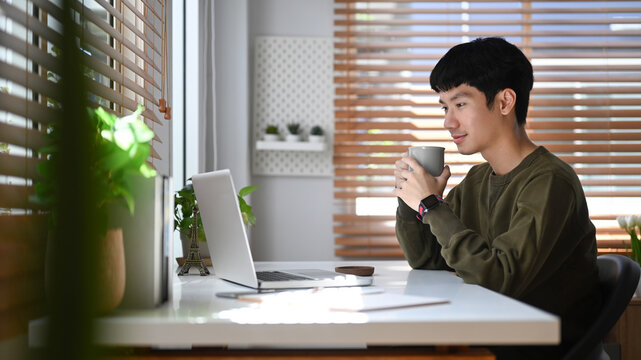Focused asian businessman watching online webinar on laptop during remote working from home