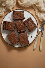 Delicious homemade chocolate brownies served on white plate over beige background