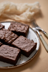 Delicious homemade chocolate brownies served on white plate over beige background