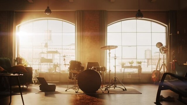 Establishing Shot: Music Rehearsal Studio in Loft Room with Drum Set in the Middle. Stylish Interior with Two Big Windows, Cozy Sofa, Shelves and Plants. Sunny Bright Day and Urban View. Zoom In Shot.