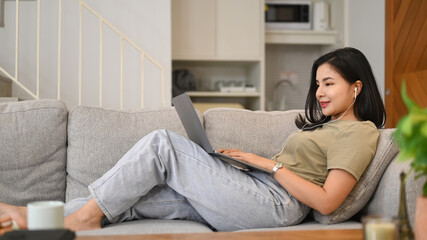 Fototapeta premium Pleasant young asian woman surfing internet, chatting in social networks on laptop computer