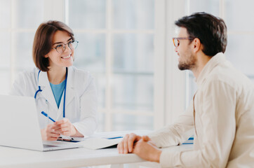 Attentive female doctor explains diagnosis to patient, gives professional consultancy, points with...