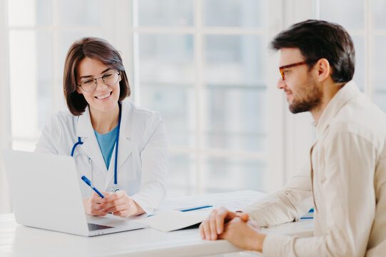 Caring Woman Doctor Gives Prescriptions To Patient, Sit Together At Table And Look At Laptop Computer, Fill Up Application Form Online. Sick Man Visit Healthcare Clinic, Gets Medical Consultancy