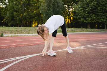 Child girl stretching on a sports track before running