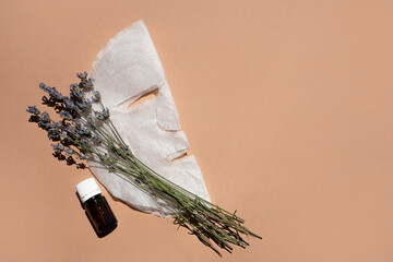 Fabric face mask, organic oil vial and lavender bouquet on beige background. Flat styling, space for text.