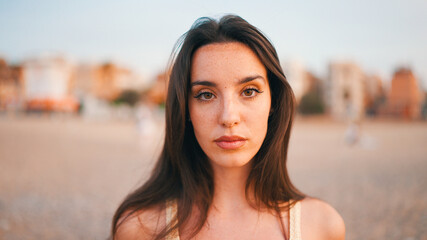 Beautiful brown-haired woman with long hair sits on the beach. Gorgeous girl with freckles and long...