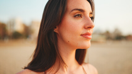 Beautiful brown-haired woman with long hair is stands on the beach. Gorgeous girl with freckles and long eyelashes.