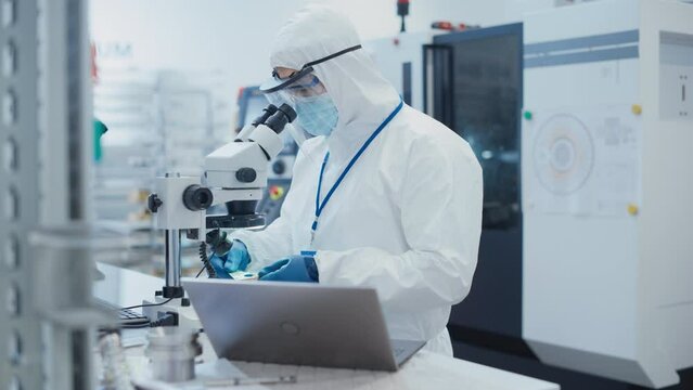Modern Technology Concept: Engineer in Coverall Working on Laptop Computer, Examining a Circuit Board with Microchips Through a Microscope. Technician Testing New Electrical Equipment.