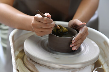 Close up view of young woman wearing apron creating handmade ceramic bowl in pottery workshop
