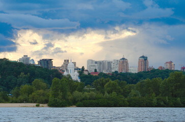 Obraz premium Panoramic landscape cityscape of Kyiv. Modern multi-story apartment buildings on horizon. Stormy sky and gloomy clouds. River Dnipro on foreground. Travel and tourism concept