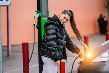 Obraz na płótnie Canvas Young beautiful woman traveling by electric car having stop at charging station