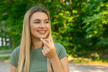 Young beautiful woman wearing green t shirt over holding an invisible aligner. Dental healthcare...