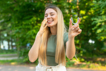 Fototapeta premium Beautiful smiling woman is holding an invisalign bracer with green background