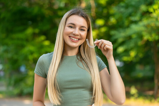 Woman with white smile, using removable braces. Closeup of beautiful happy smiling woman holding invisible braces, Teeth Trainer. Dental Treatment, Health Concept