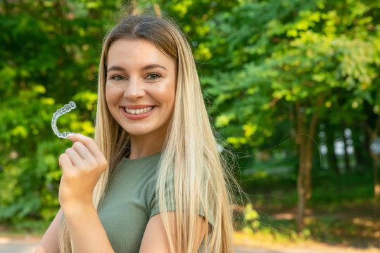 Taking care of teeth. Close up of clear aligners in hands of happy girl who is standing and showing orthodontic device to the camera. Selective focus and isolated background