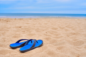 Men's rubber flip-flops stand on beautiful yellow sand. The concept of recreation in hot countries. Women's flip-flops against the backdrop of the blue sea and sand. relax on the beach. - Powered by Adobe