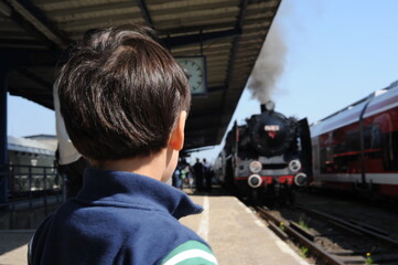A young boy standing at the train station platform and looking at the locomotive train approaching