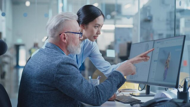 Factory Office Facility: Industrial Engineers Drafting Blueprints of a Heavy Industry Machine Parts on a Computer CAD Software. Asian Female Technician Discusses Work with Middle Aged Designer.
