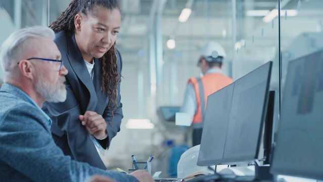 Factory Office Facility: Industrial Engineers Drafting Blueprints of a Heavy Industry Machine Parts on a Computer CAD Software. African American Technician Discusses Work with Middle Aged Designer.