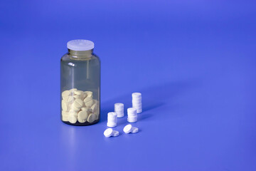 White pills, medical tablets, placebo or vitamins and brown transparent bottle with medicine on dark blue background closed up, vertical plane, copy space on the right