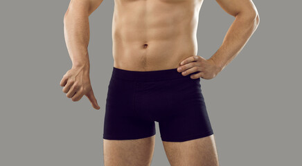 Guy in underwear showing thumbs down standing isolated on grey background. Young male has trouble...