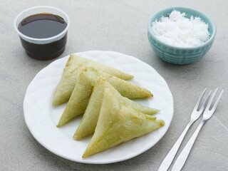 Lupis or Lopis, a traditional Indonesian food made from sticky rice and wrapped in banana leaves. Served with grated coconut and liquid brown sugar. Selective focus image.
