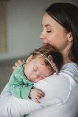 Young beautiful dark-haired mother holds her newborn daughter in her arms in a cozy home. Family portrait. Motherhood. Young woman kisses her 2 month old baby.