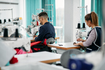 Rear view of textile workers sewing at production line in factory.