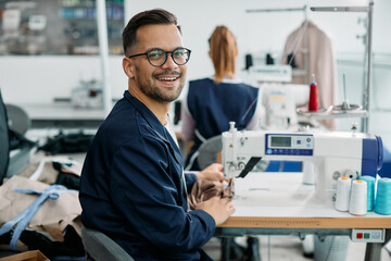 Fototapeta premium Happy man working as tailor in textile factory and looking at camera.