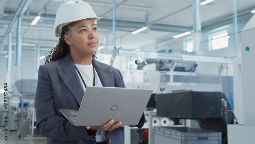 Poster Portrait of a Black Female Engineer in Hard Hat Standing and Using Laptop Computer at Electronic Manufacturing Factory. Technician Thinking About Daily Tasks and Working on Project Pipeline.