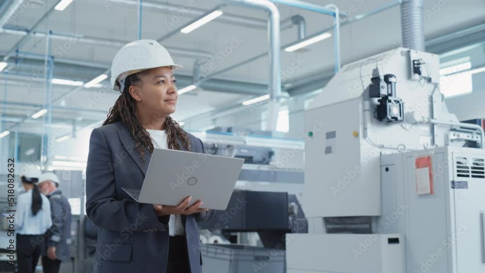 Poster portrait of an african female engineer in hard hat standing and using laptop computer at electronic 