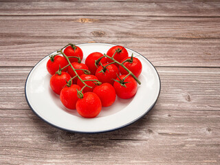 Ripe red cherry tomatoes on a white dish on a wooden table