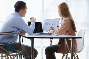 Man sits in wheelchair and brainstorms with colleagues, male and female employees working together in the office, working as a team in a large organization. The concept of team management is diverse.