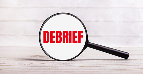 The magnifying glass stands vertically on a light background with the text DEBRIEF