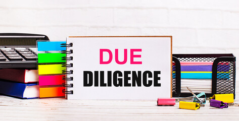 On a light wooden background, a calculator, multi-colored sticks and a notebook with the text DUE...