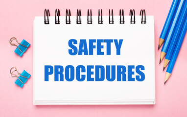 On a light pink background, light blue pencils, paper clips and a white notebook with the text SAFETY PROCEDURES