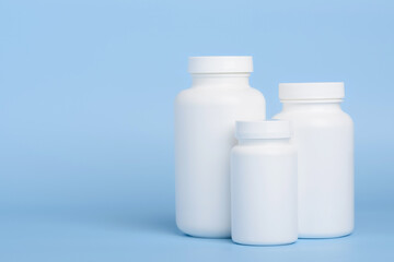 Three blank white plastic bottles of medicine pills or supplements on blue background with side copy-space - 518086433