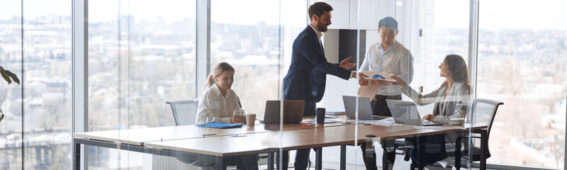 People standing near table, team of young businessmen working and communicating together in office.