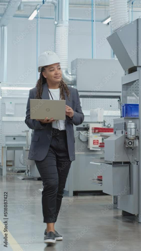Aufkleber vertical screen: black african female engineer in hard hat walking and using laptop computer at elec