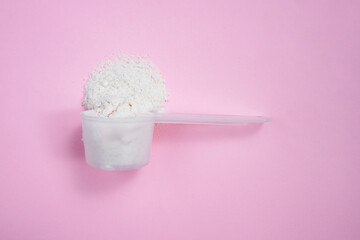 Measuring spoon with collagen powder on a pink background. Side view, space for text.
