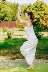 Young woman practices yoga in the summer garden - Garudasana or Eagle Pose