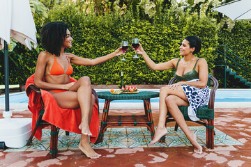 Multiethnic women in bikini celebrate toasting with red wine poolside in the summer