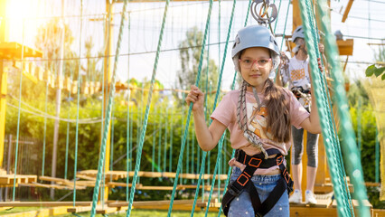 A brave young Caucasian girl in a helmet and insurance, climbing a rope town, in an amusement park...