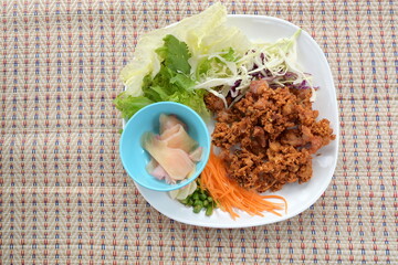 Deep fried sour chicken tendons served in a white plate with small cup pickled ginger,carrots,peppers, garlic, cabbage and other fresh vegetables placed on woven mat. It is a popular appetizer.
