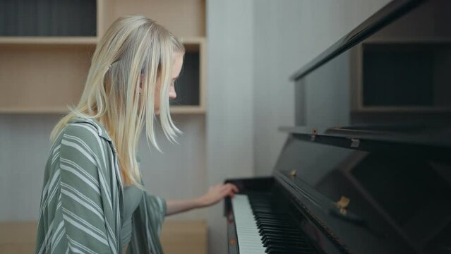Teenage girl with blonde hair studying to play the piano at home in slow motion. Education, skills concept.