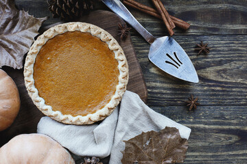 A whole fresh baked pumpkin pie over wood background with ripe pumpkins, cinnamon and star of...