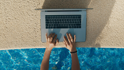 Top view on young female hands type text on laptop keyboard, lay or sit in swimming pool on work away vacation. People addicted to work, workaholics. 