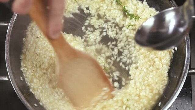 Preparing of delicious risotto in the frying pan.Pouring of broth.